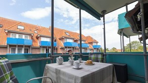 A balcony with a table set for tea, chairs, and a view of a row of houses with blue awnings.