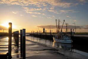 Eine Anlegestelle mit einem angedockten Boot, ein Leuchtturm im Hintergrund und ein Sonnenuntergang über dem Wasser.