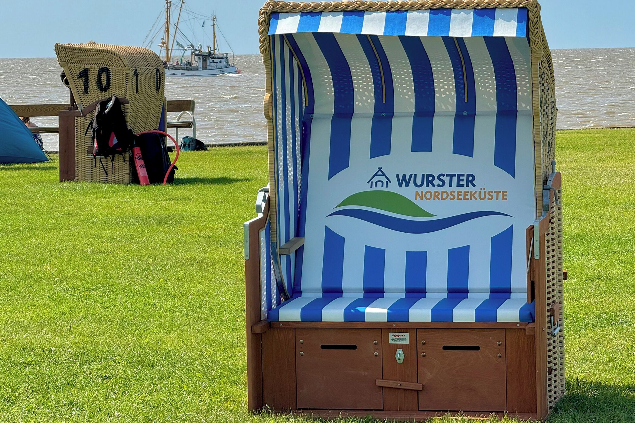 Edifici de fusta al costat de la platja, amb un toldo a ratlles i el text "WURSTER NORDSEEKÜSTE".