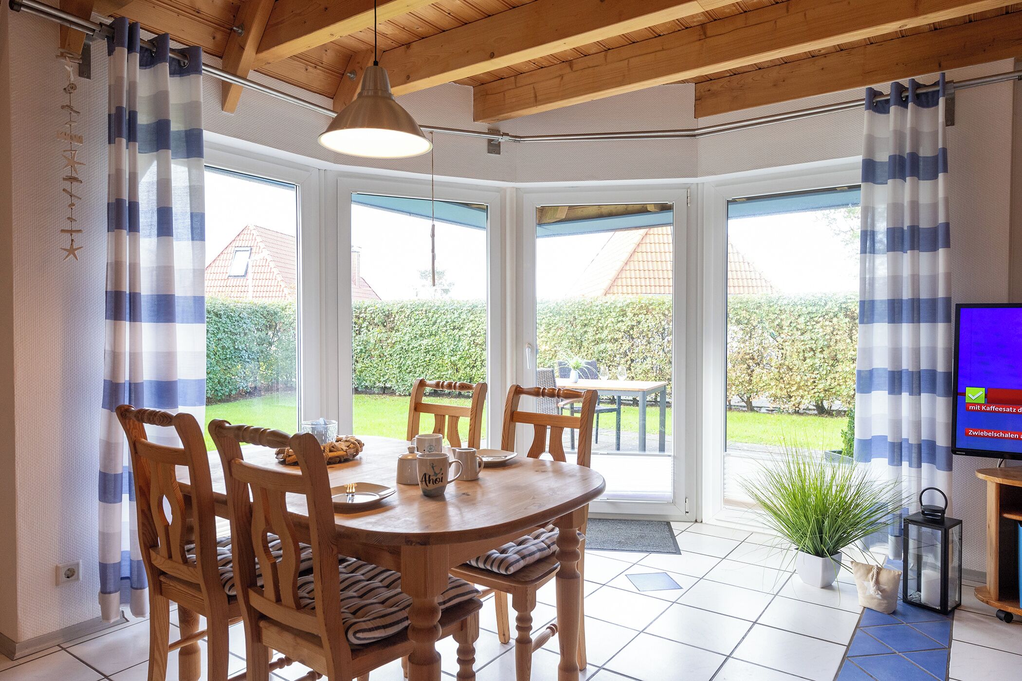 A dining area with a wooden table and chairs, a hanging light fixture, and a view of the garden through large windows.