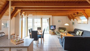 A spacious living area with a high ceiling, wooden beams, a dining table with chairs, a sofa, and a television.