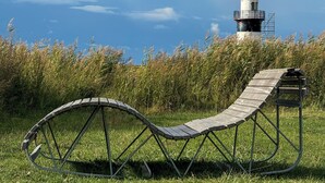 A curved wooden bench in a grassy field with a lighthouse in the background.