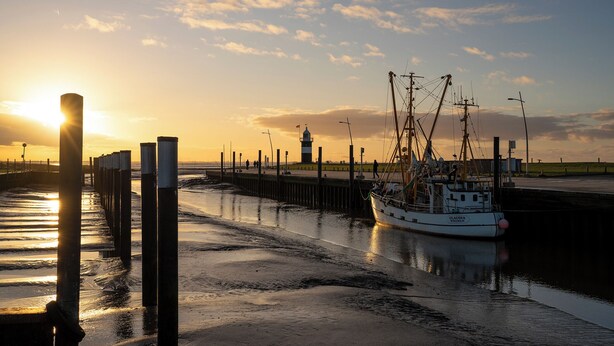 A pier with a boat docked, a lighthouse in the background, and a sunset over the water.