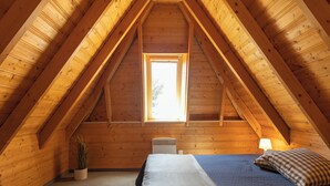 Une pièce avec un plafond en bois incliné, une fenêtre, un lit avec un matelas bleu, une lampe de chevet et une plante en pot.