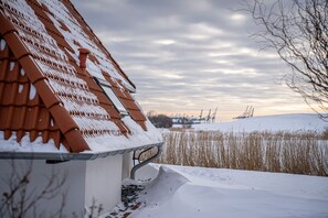 Ein Gebäude mit geneigtem, schneebedecktem Dach, blauem Himmel und einer entfernten Aussicht auf Kräne auf einem Hügel.