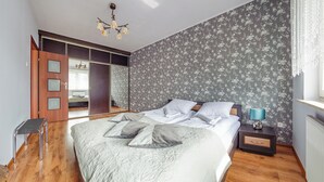 A bedroom with a large bed, a nightstand with a lamp, a wooden floor, a wardrobe with a mirror, and a door leading to another room. - Apartament Sun & Snow Siedleckiego 8 (Wladyslawowo)