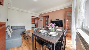 A dining area with a wooden table set for four, a grey sofa, and a TV mounted on the wall. - Apartament Sun & Snow Siedleckiego 8 (Wladyslawowo)