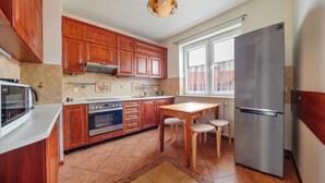 A kitchen with wooden cabinets, a stainless steel refrigerator, a microwave, an oven, and a dining table with two chairs. - Apartament Sun & Snow Siedleckiego 8 (Wladyslawowo)
