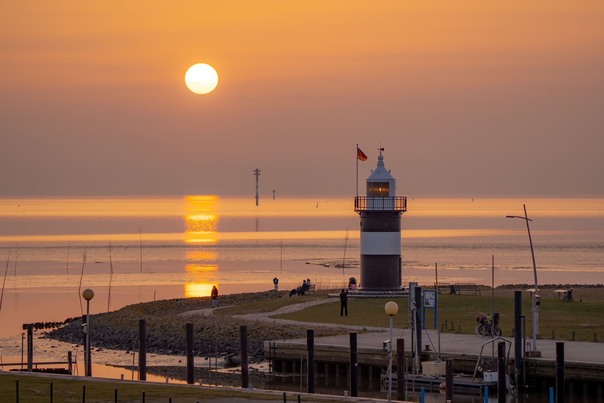 A lighthouse with a flag, a calm sea, and a sunset.