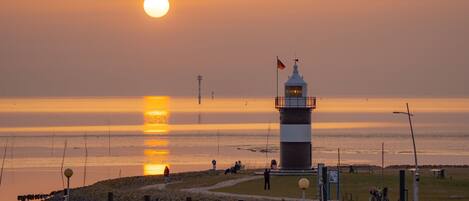 A lighthouse with a flag, a calm sea, and a sunset.