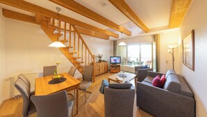 A modern living room with a wooden staircase, a dining area, and a seating area with a sofa and armchairs.