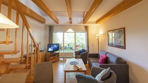 A spacious living area with a wooden staircase, a television, a dining table, and a sofa.