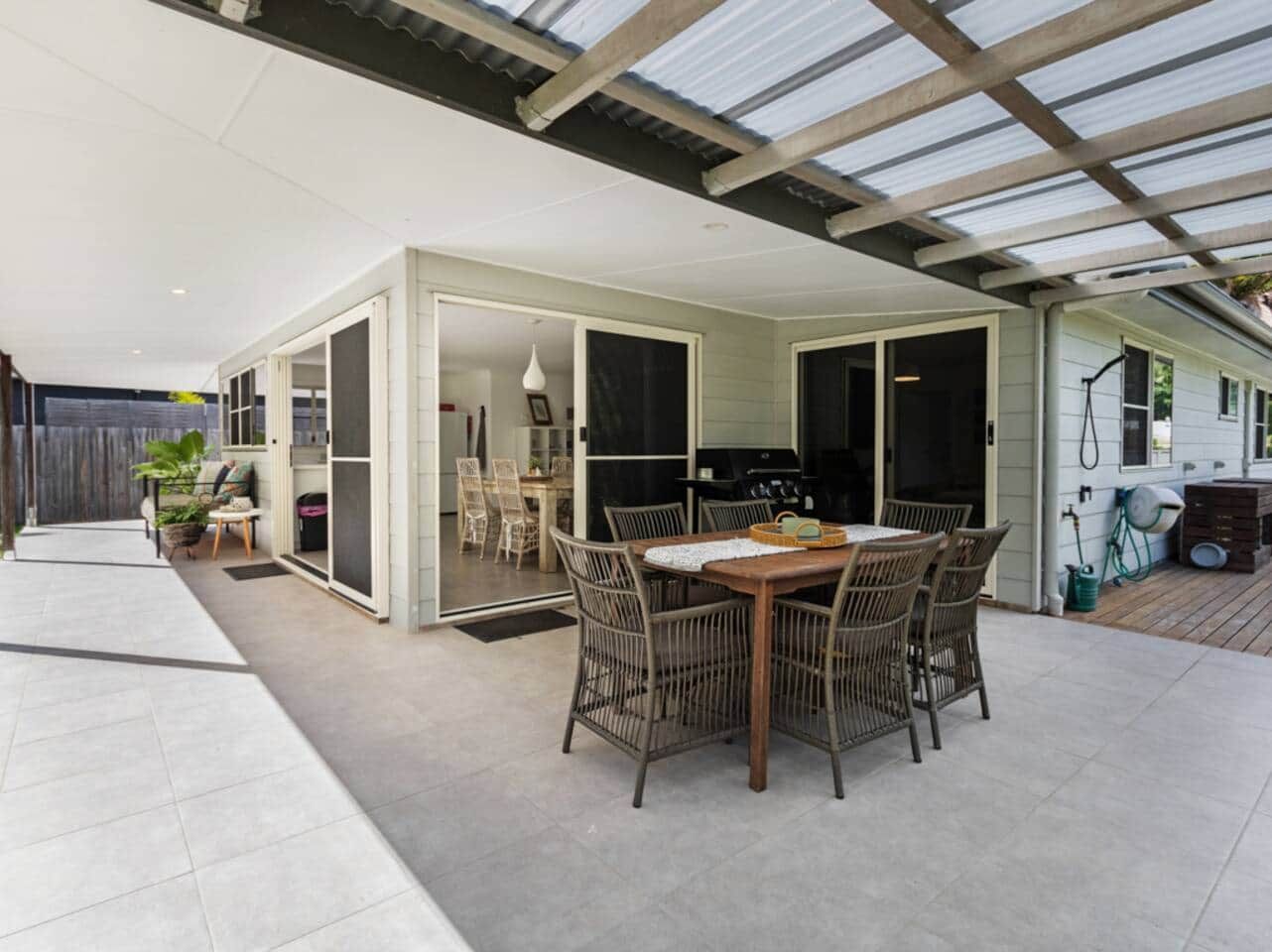 A covered outdoor dining area with a table and chairs, a grill, and a sliding glass door leading to an indoor space.