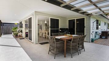 A covered outdoor dining area with a table and chairs, a grill, and a sliding glass door leading to an indoor space.