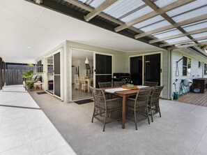 A covered outdoor dining area with a table and chairs, a grill, and a sliding glass door leading to an indoor space.