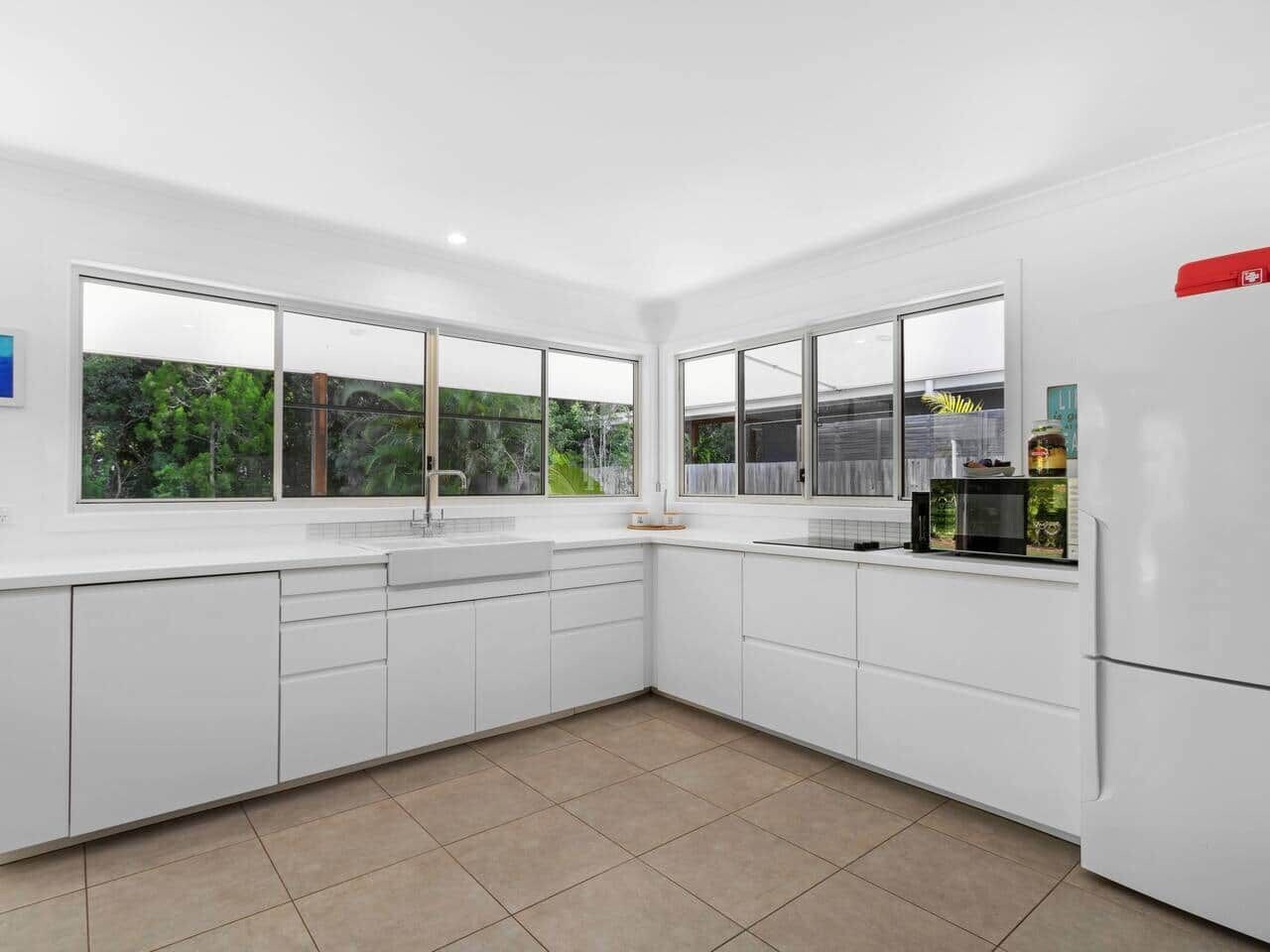 A modern kitchen with white cabinetry, a refrigerator, and a window overlooking greenery.