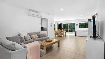 Uma sala de estar moderna com um sofá cinza, uma mesa de centro de madeira e uma televisão em um móvel.