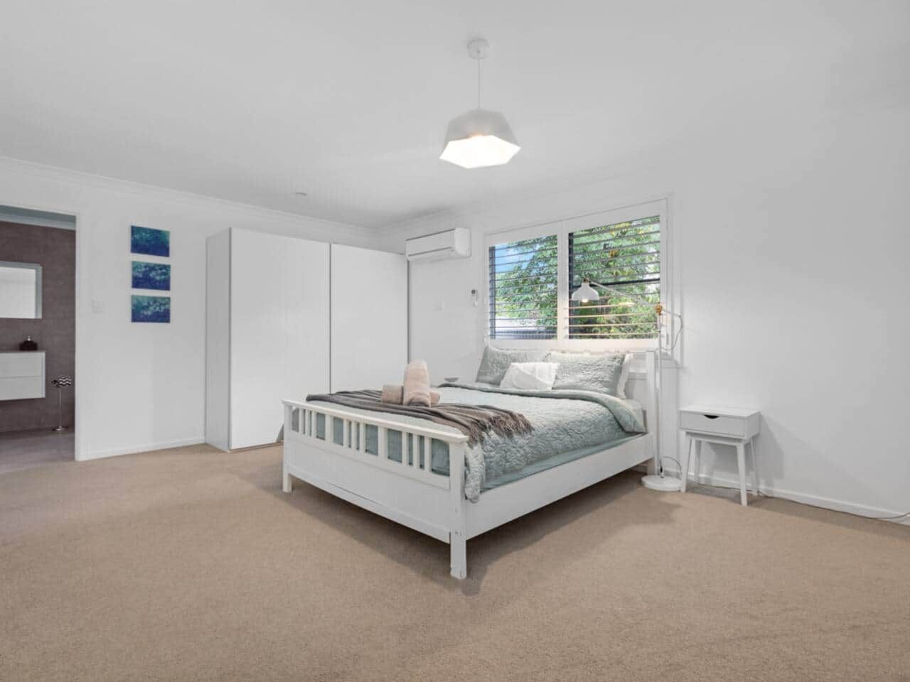 A bedroom with a bed, a bedside table, a wardrobe, and a window with blinds.