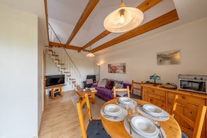 Un espace de vie moderne comprenant un escalier en bois, un coin repas avec des tables, un canapé et un espace cuisine.