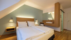 A bedroom with a large bed, a nightstand, a wall-mounted shelf, a mirror, and a door.