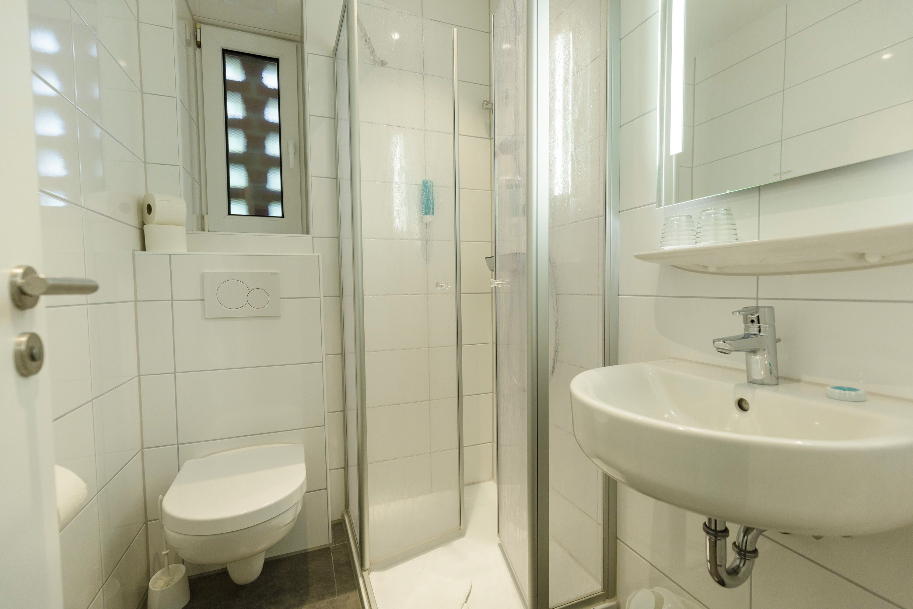 Ein modernes Badezimmer mit Toilette, einer in Glas abgeschlossenen Dusche und einem Waschbecken mit Spiegel darüber.