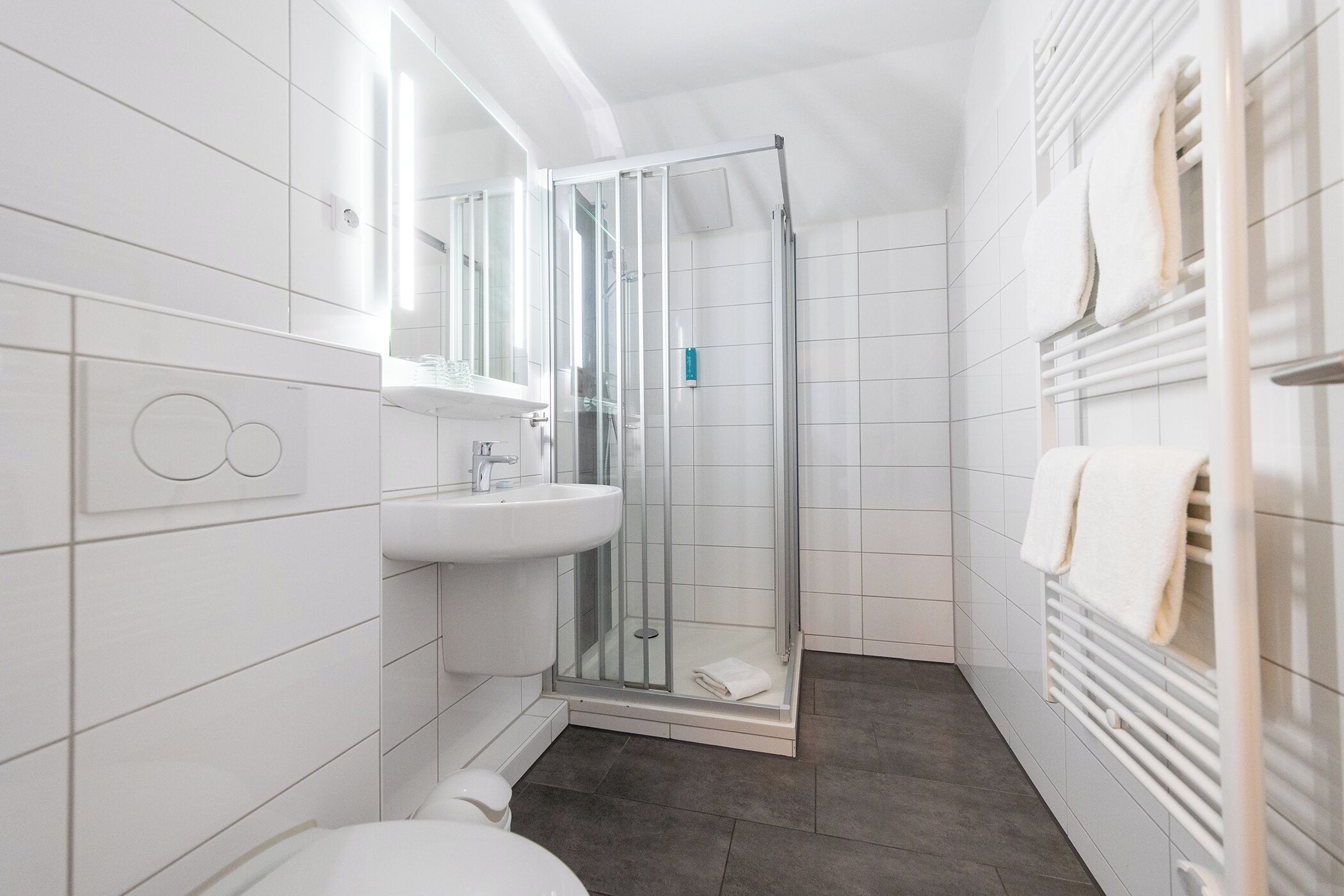 Ein modernes Badezimmer mit Duschkabine aus Glas, einem weißen Waschbecken und einem Handtuchhalter.
