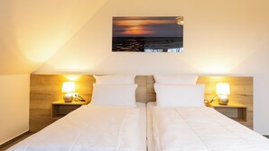 Ein Hotelzimmer mit einem Bett, zwei Nachttischen mit Lampen, einem Holz-Kopfteil und einem Sonnenuntergangsbild an der Wand.