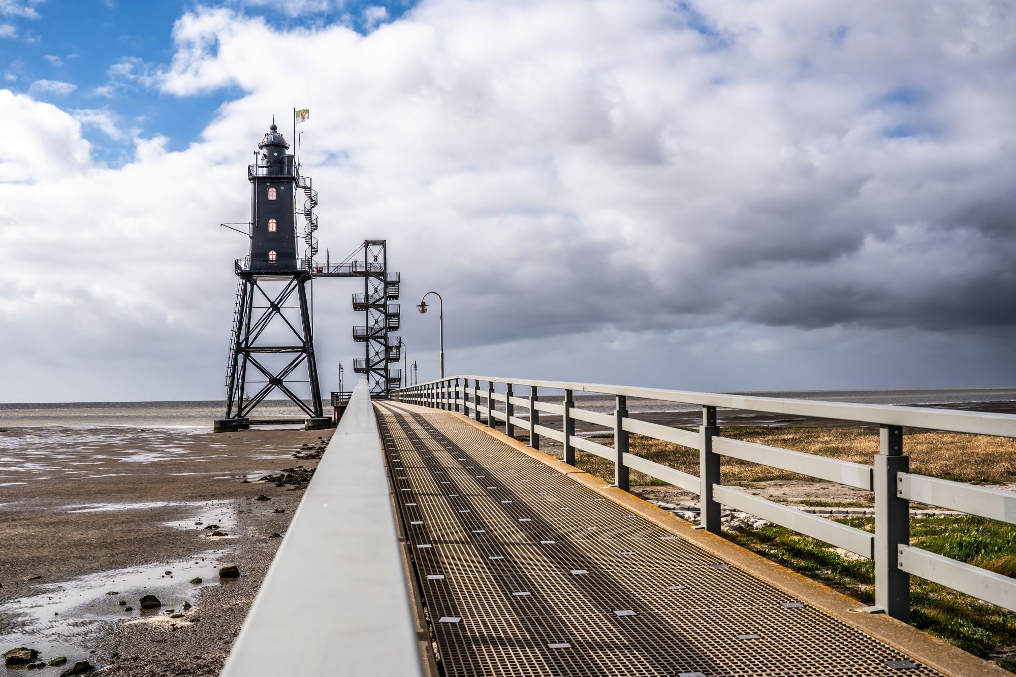 Ein Leuchtturm mit einem zu ihm führenden Weg, umgeben von einer grünen Fläche und einem bewölkten Himmel.