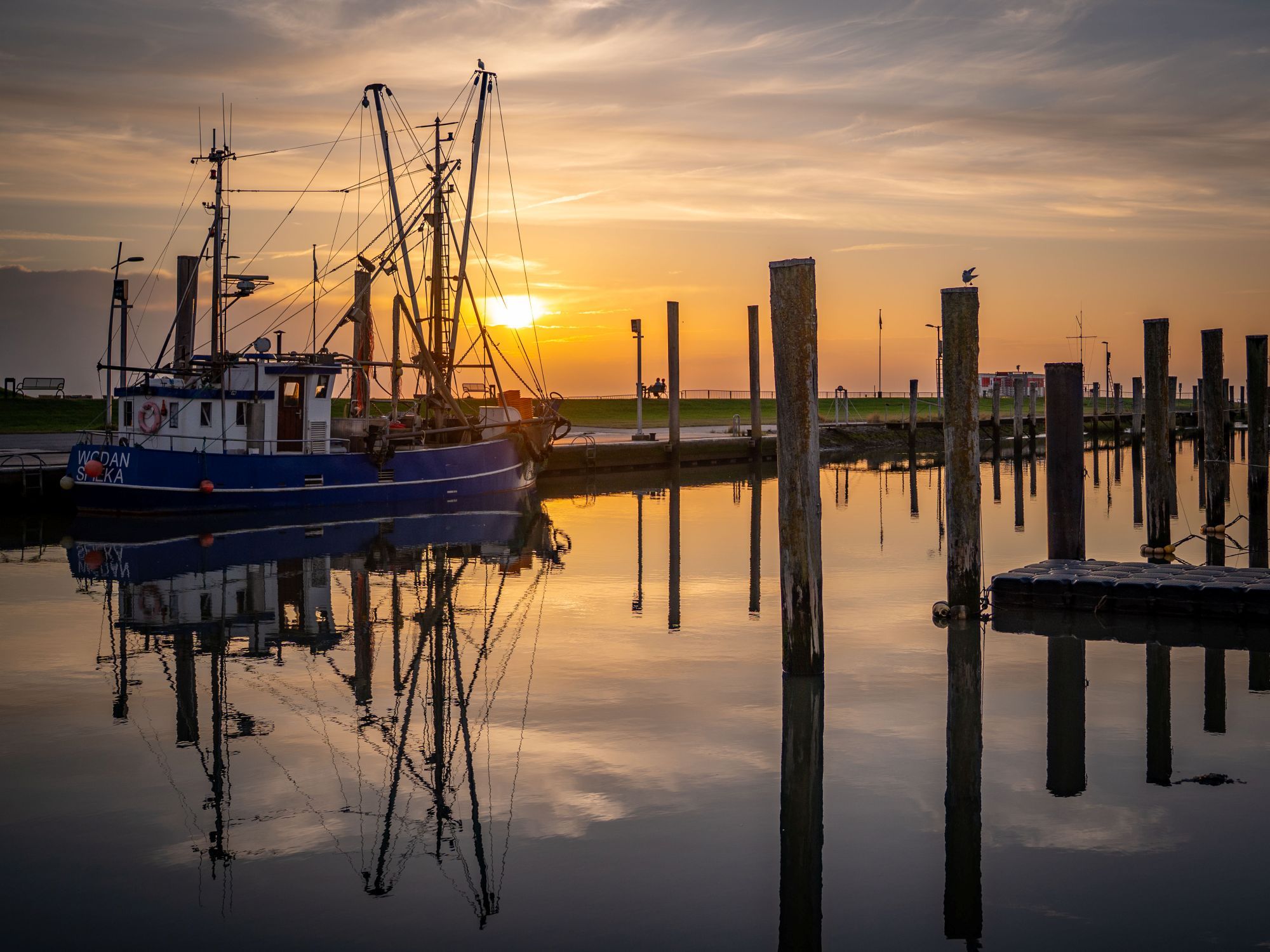 Een boot aangemeerd aan een steiger, met een zonsondergang op de achtergrond.