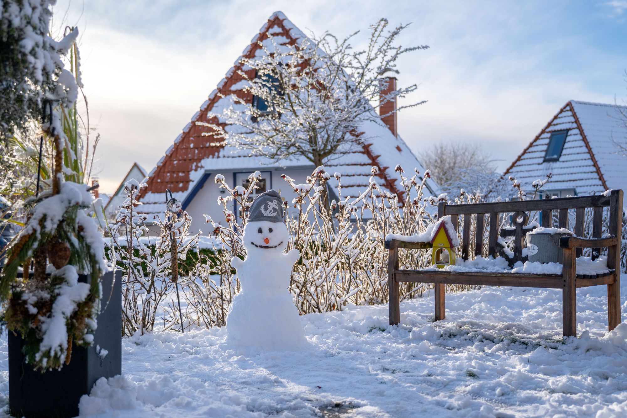 Ein Schneemann in verschneiter Winterlandschaft, im Hintergrund Häuser.