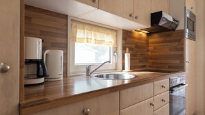Une cuisine moderne avec des meubles en bois, un four encastré, une machine à café et une fenêtre avec un rideau.