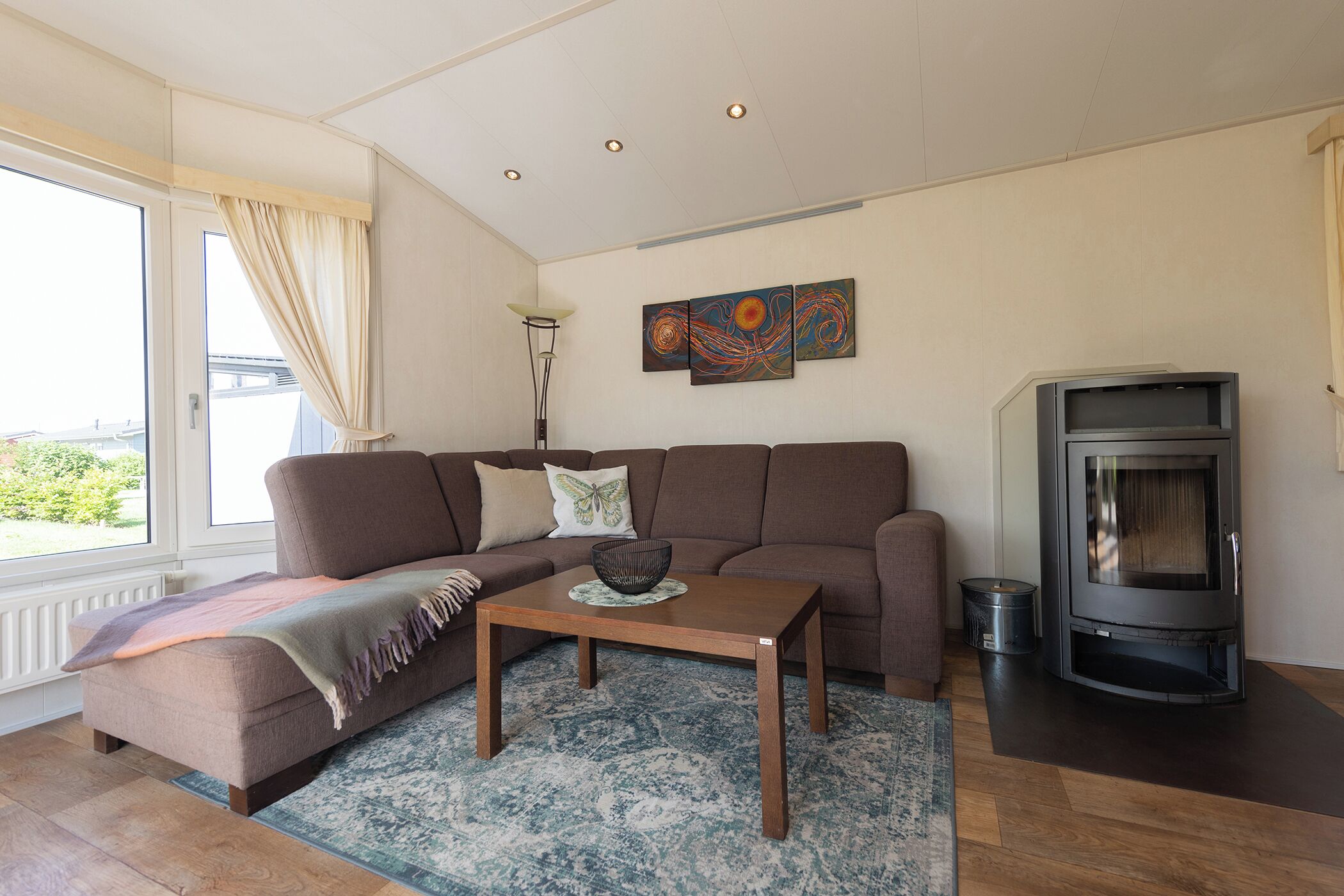 Ett modernt vardagsrum med en soffa, ett soffbord, en öppen spis och ett stort fönster med gardiner.