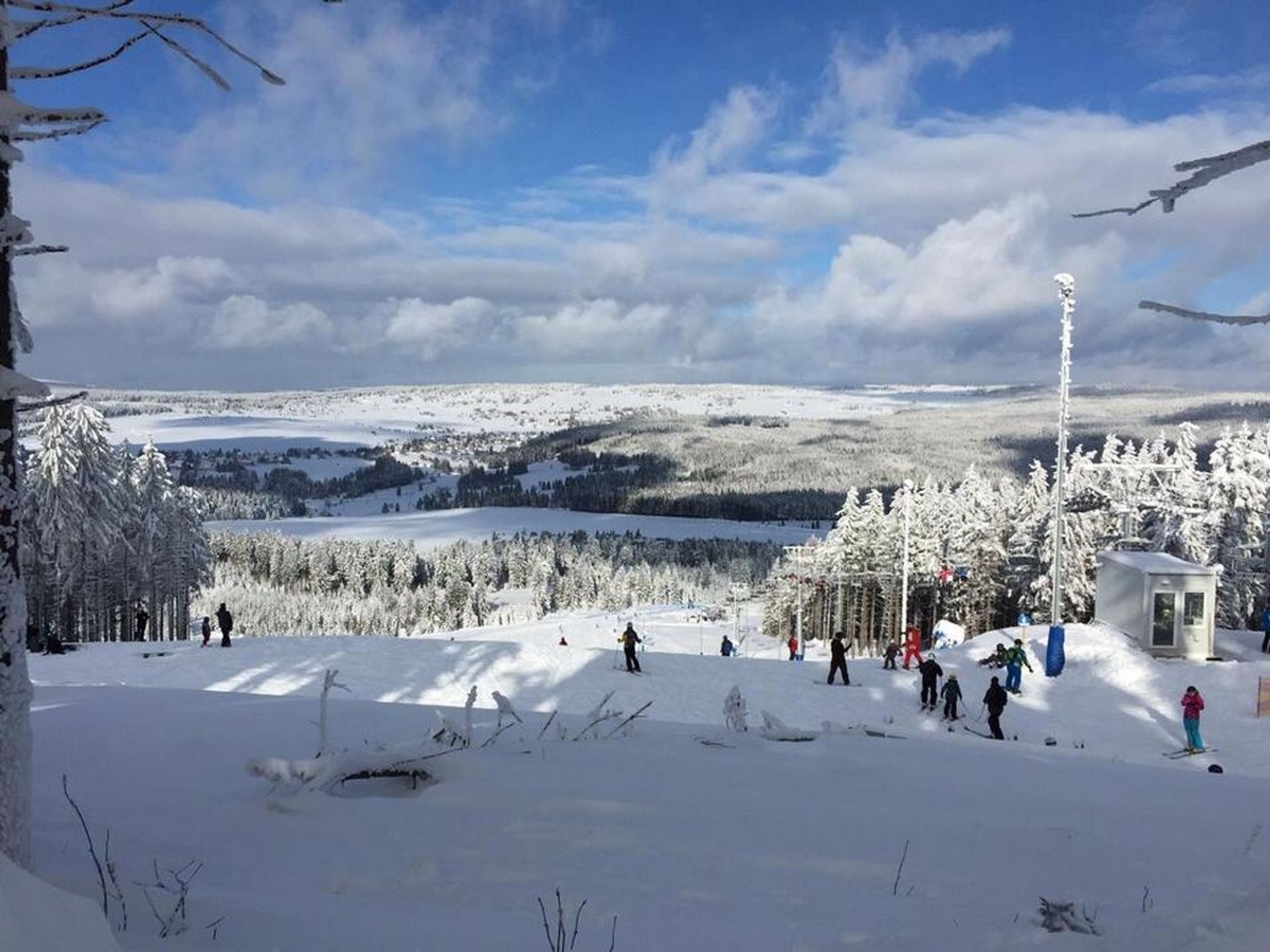 Ein verschneiter Skipisten mit Skifahrern und einer kleinen Berghütte.