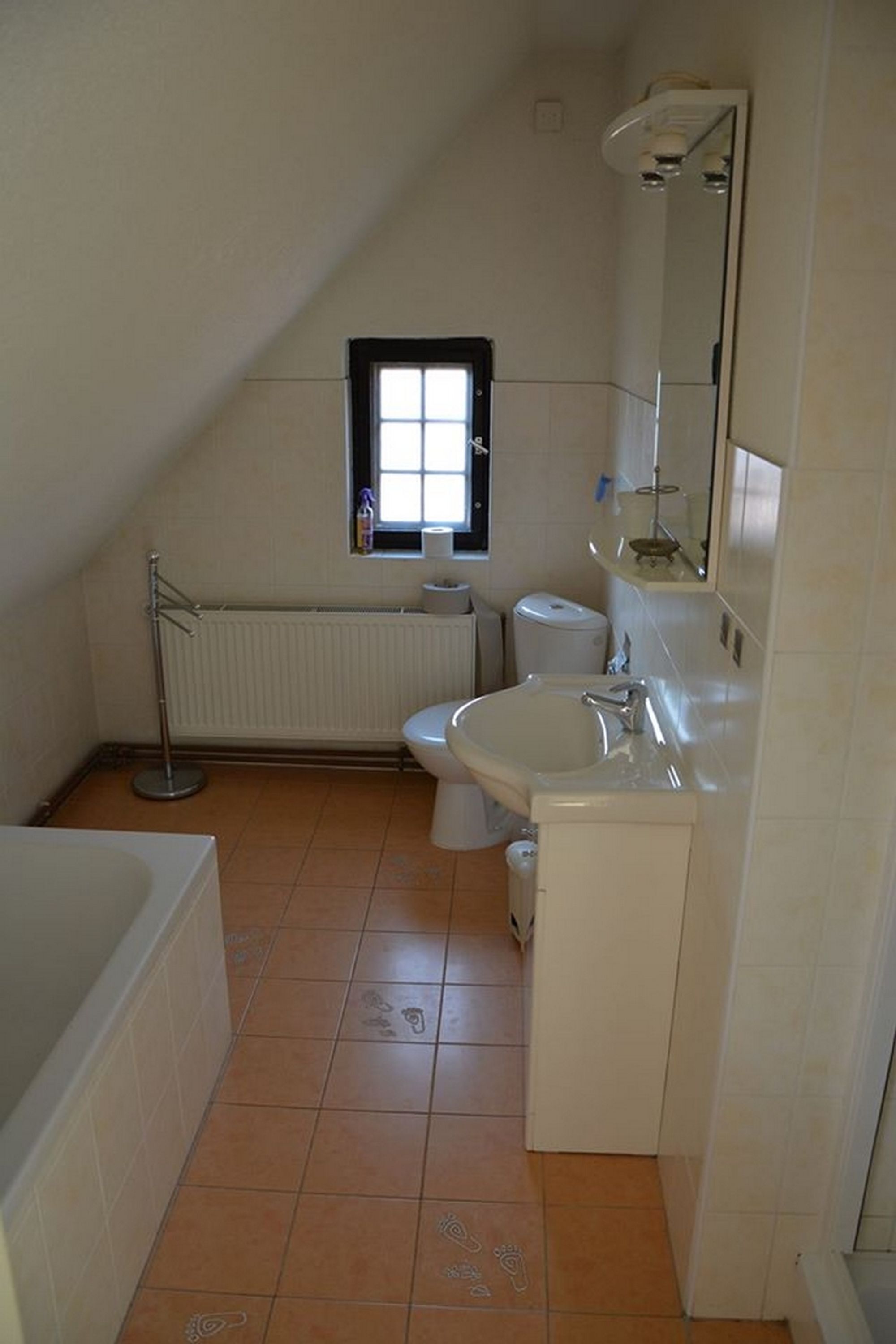 A small, clean bathroom with a window, a radiator, a toilet, and a sink.