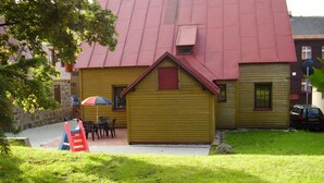 A yellow building with a red roof, a small porch with a table and chairs, and a playground in the foreground. - Holiday Home Abertamy (Abertamy)