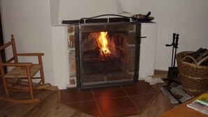 A fireplace with a fire, a wooden rocking chair, and a basket of firewood. - Holiday Home Abertamy (Abertamy)