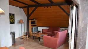 A cozy living room with a wooden ceiling, a television, a red sofa, and a small table with a vase. - Holiday Home Abertamy (Abertamy)