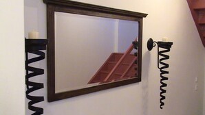 A mirror with a wooden frame on a white wall, a candle holder, and a spiral light fixture. - Holiday Home Abertamy (Abertamy)