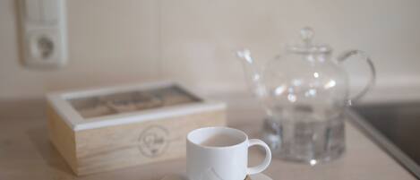A white cup on a saucer with a spoon, a glass teapot, and a wooden box with a picture on a table.