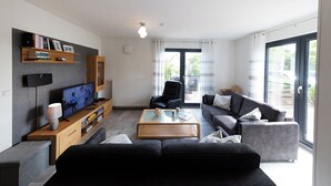 A modern living room with a TV, sofa, and coffee table. - Vacation home Möwennest. With sun terrace and at ground level. (Wurster Nordseeküste)