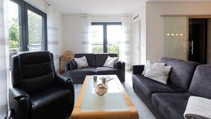 A modern living room with a leather sofa, a glass coffee table, and a black leather armchair. - Vacation home Möwennest. With sun terrace and at ground level. (Wurster Nordseeküste)