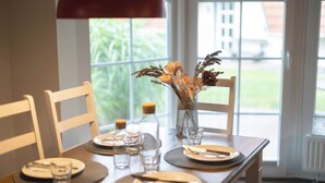 Une table à manger dressée avec des assiettes, des couverts et un vase contenant des fleurs séchées.