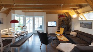 Un vaste espace de vie doté d’un plafond en bois, d’une table à manger avec des chaises, d’un canapé et d’un téléviseur.