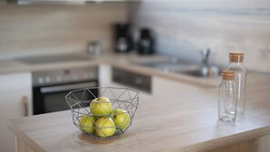 Un comptoir de cuisine sur lequel se trouve un panier en fil métallique contenant des pommes, ainsi que deux bouteilles en verre vides, fermées par des bouchons en liège.
