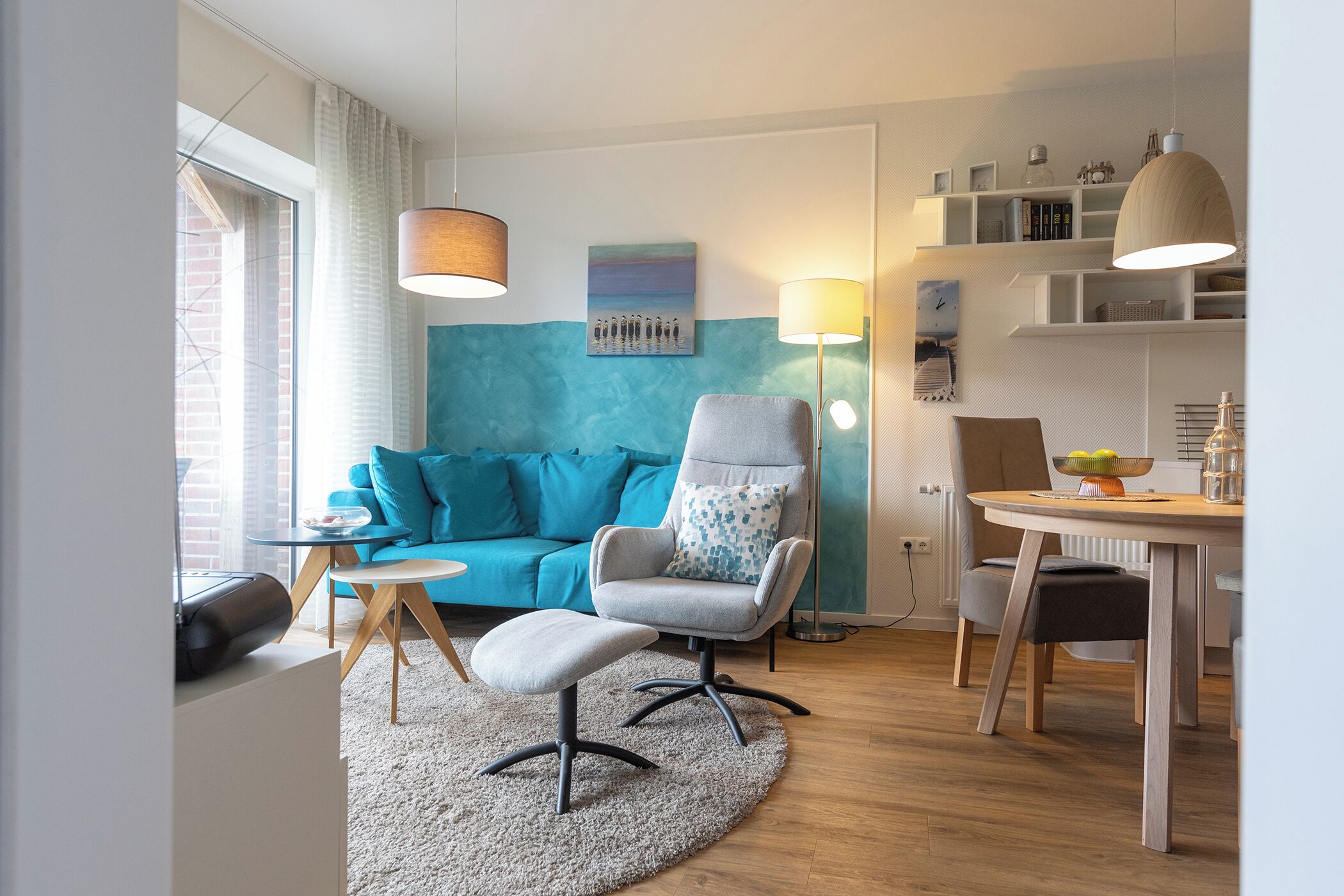 A modern living room with a blue sofa, a grey armchair, a round coffee table, and a dining area with a white table and chairs.