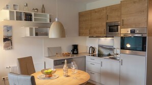 Une cuisine moderne avec des meubles en bois, un four encastré et un coin repas comprenant une table ronde et des chaises.