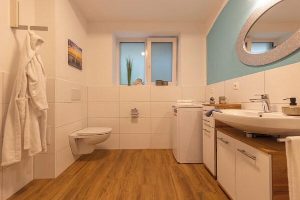 A modern bathroom with a toilet, a washing machine, a sink, and a mirror.