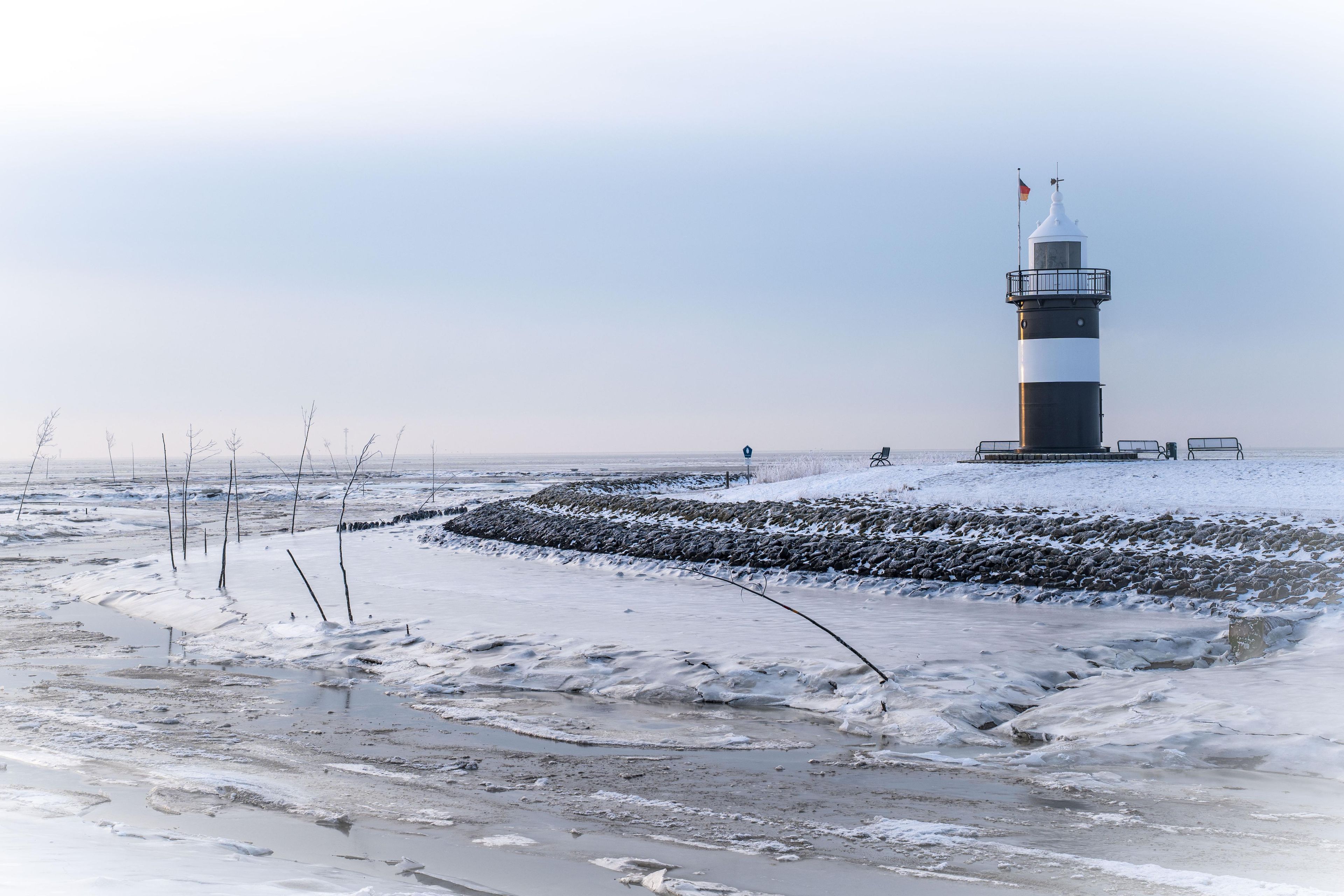 A lighthouse on a snowy beach with a clear sky.
