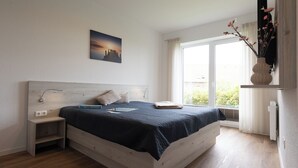 A bedroom with a bed, bedside tables, a nightstand, a window with curtains, and a wall-mounted TV.