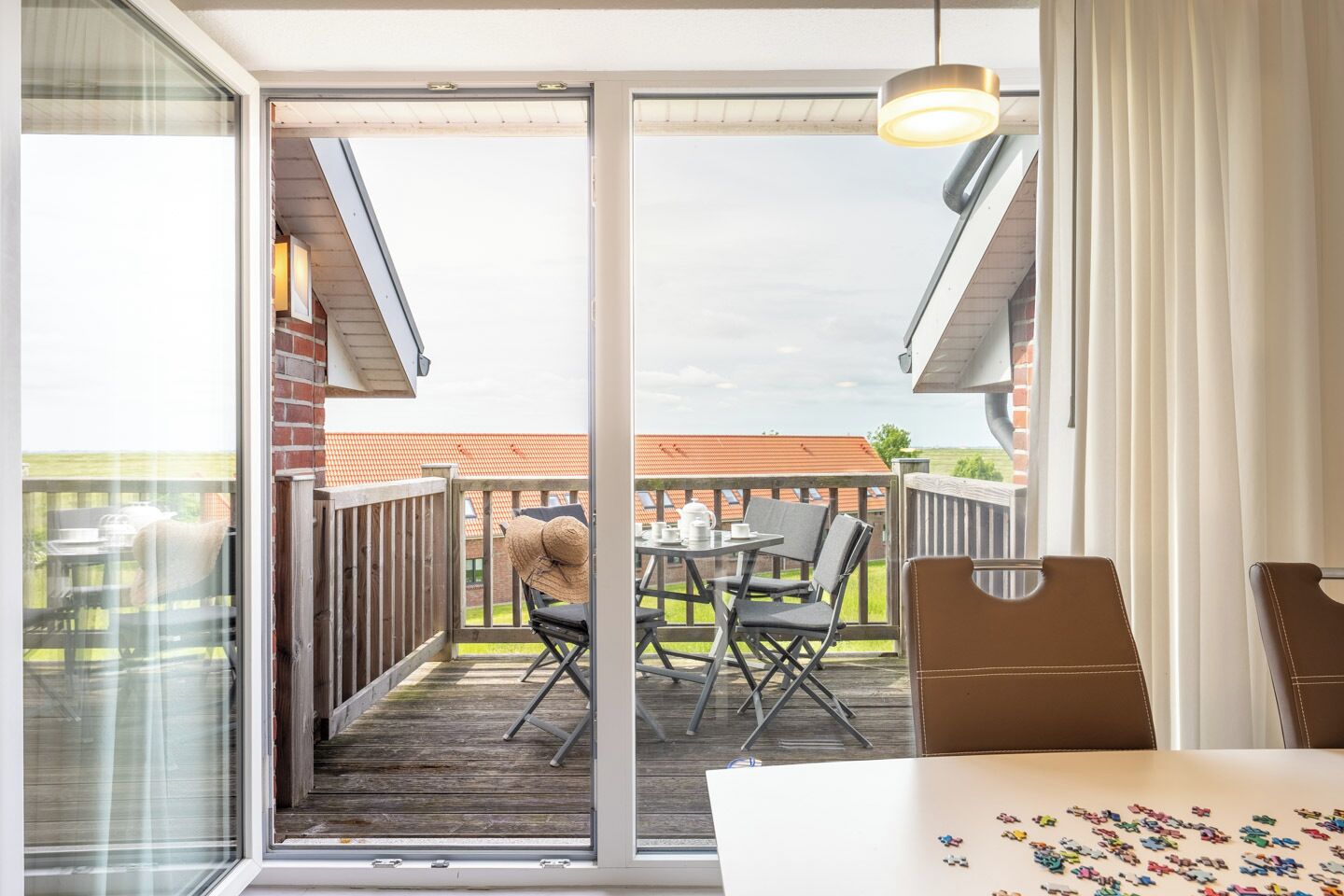 En balkon med et bord og stole, en hængende lampe samt udsigt til en murstensbygning.
